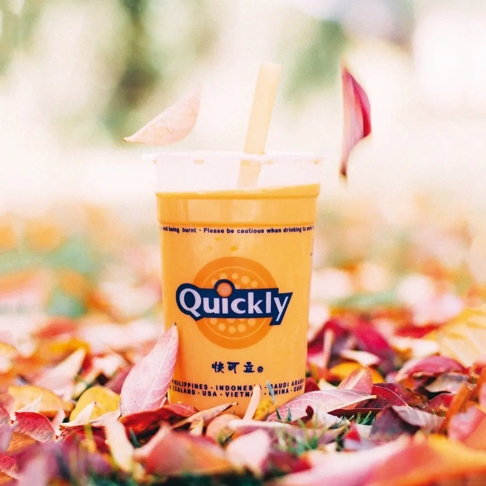 Vibrant orange smoothie amidst colorful autumn leaves at Quickly Stoneridge Mall, a Fast Food Restaurant in Pleasanton
